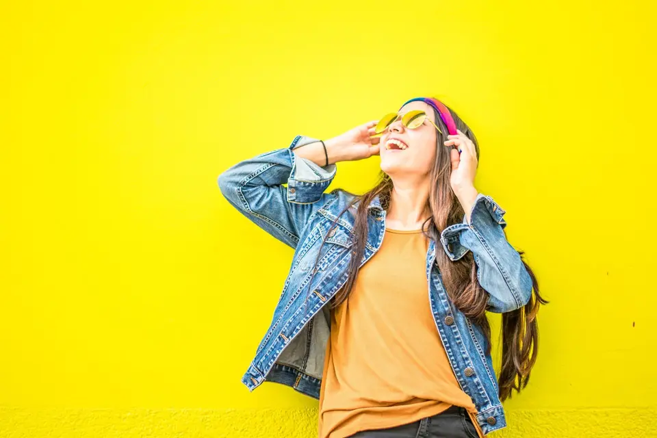 Personne souriante en blazer terracotta devant un mur jaune
